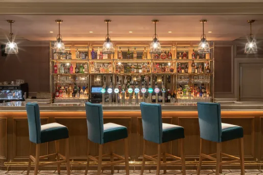 Bar counter with blue, cushioned chairs with alcohol along the shelves on the walls