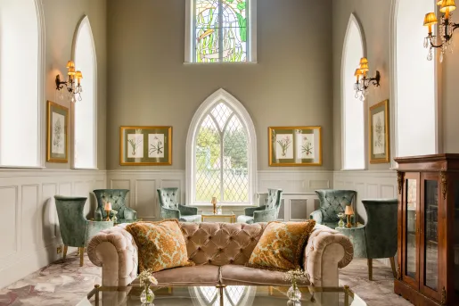 Lounge with cushioned green and red sofas and large, stained glass windows in the background