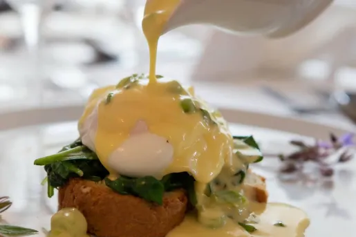 Plate of eggs benedict, while pouring sauce over