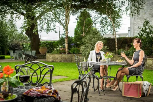 Two women sitting outdoors in a garden, holding up glasses of wine