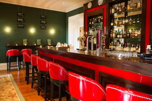 Bar and lounge with a wooden counter and red, leather stools