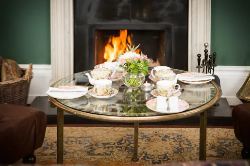 Coffee table with teacups and coasters on top, in front of a fireplace