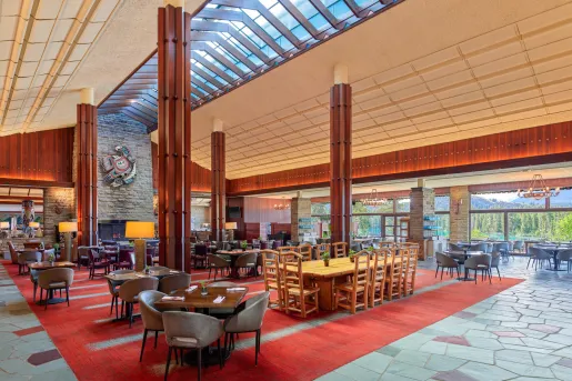 Large restaurant dining hall with red carpet and wooden dining tables, and large wooden pillars
