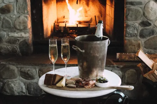 Bucket with a champagne bottle and two glasses to the left, in front of a stone fireplace