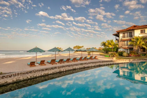 Outdoor pool with a row of reclining chairs looking out to the beach