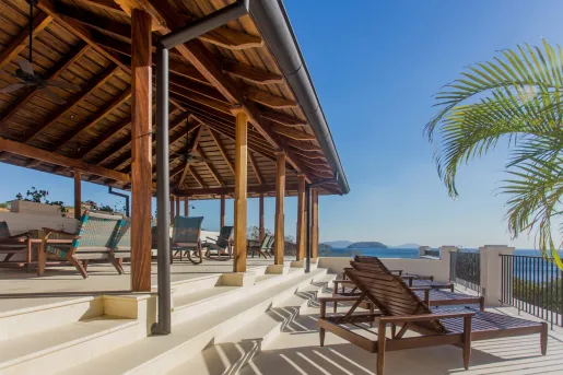Outdoor patio with wooden roofing and chairs, looking out to the ocean