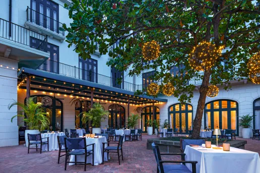 Outdoor patio next to a white building, with dining tables and lights on a tree