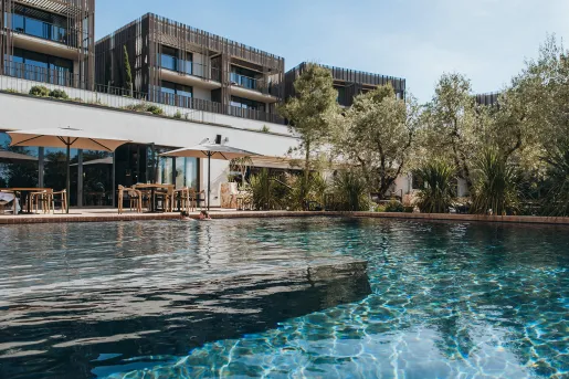 Outdoor pool surrounded by trees, with a hotel building in the background