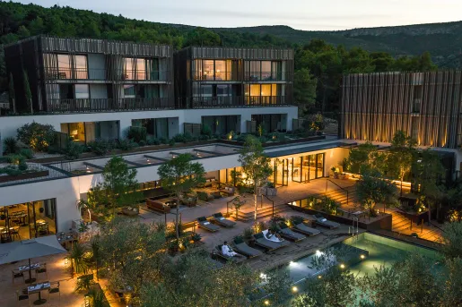 Exterior, evening view of a large hotel complex with an outdoor pool surrounded by trees