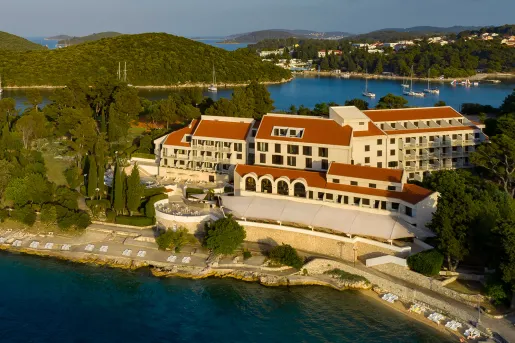 Exterior sky view of yellow and brown hotel with a lake in the background and the ocean in front