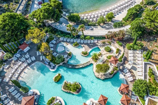 Sky view of outdoor pool surrounded by reclining chairs and the beach in the back