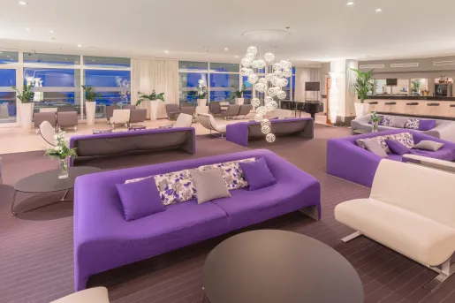 Indoor lounge with white and purple sofas and large windows in the background