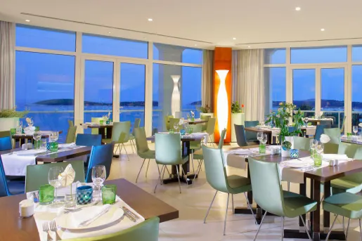 Dining hall with green chairs and wooden tables, with large windows along the walls