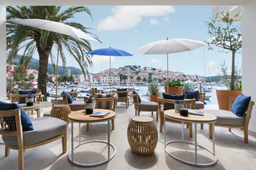 Outdoor patio with gray, cushioned chairs, gray and blue umbrellas looking out towards the ocean