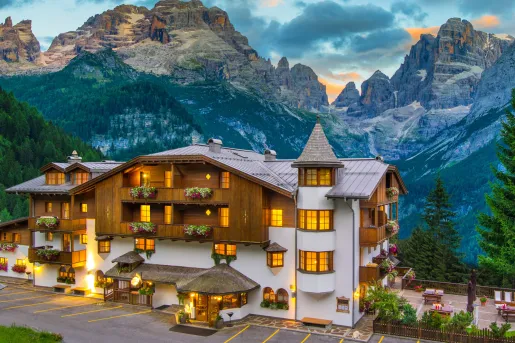 Exterior of white and brown hotel building, with large mountains in the background