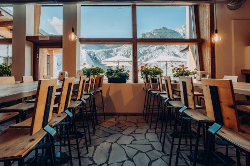 Restaurant dining hall with long tables leading to a window with potted flowers