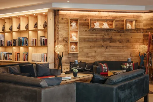 Library in a wooden cabin room, with books along the shelves and cushioned, gray couches