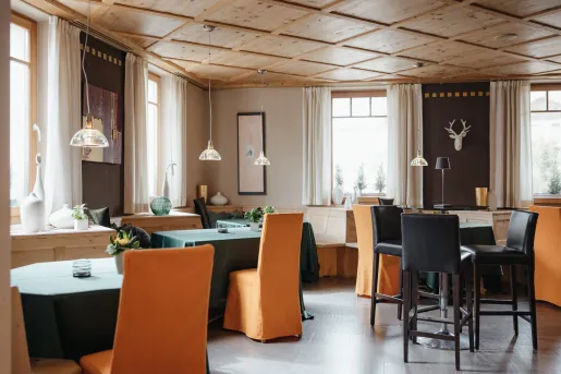 Restaurant dining hall with orange chairs and green dining tables, with art pieces on the walls