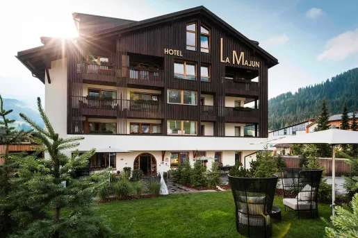 Exterior view of dark brown and white hotel building, with a small grass field in front