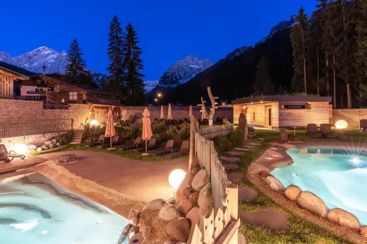 Outdoor pool area with two large hot tubs and a wooden sauna in the back