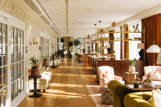 Long hallway with wooden floors, cushioned couched to the right and wooden furniture along the walls