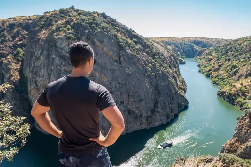 Man standing on a cliff looking down at a river