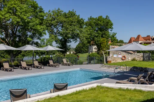 Outdoor pool surrouonded by umbrellas and reclining chairs, with a large lake in the background
