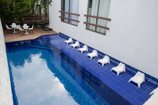 Outdoor blue pool, surrounded by white chairs and a white building to the right
