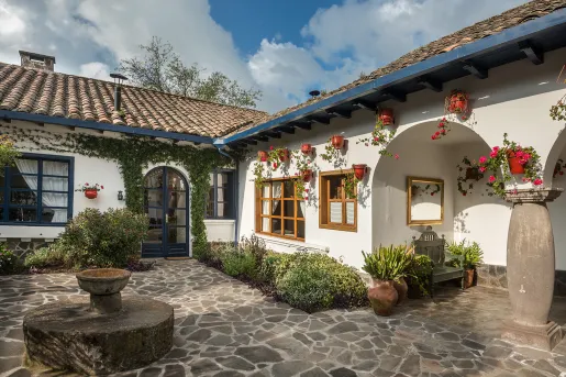 Exterior view of white building with a small fountain and stone flooring in front