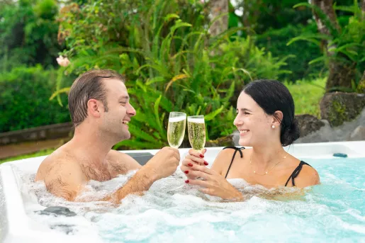 Man and woman sitting in a hot tub, clinking their glasses of champagne