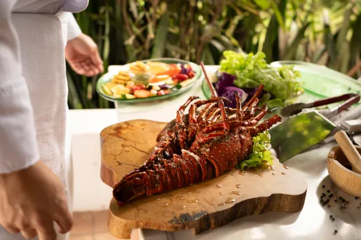 Cooked lobster on a wooden plank, with a plate of vegetables to the left