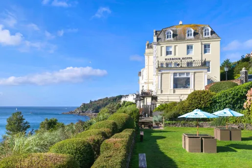 Exterior view of cream-colored building with trimmed bushes and the ocean to the left