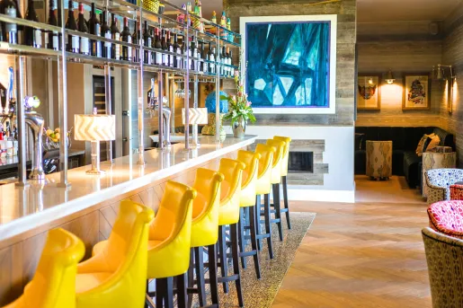 Bar and lounge with yellow bar stools and a fireplace to the right