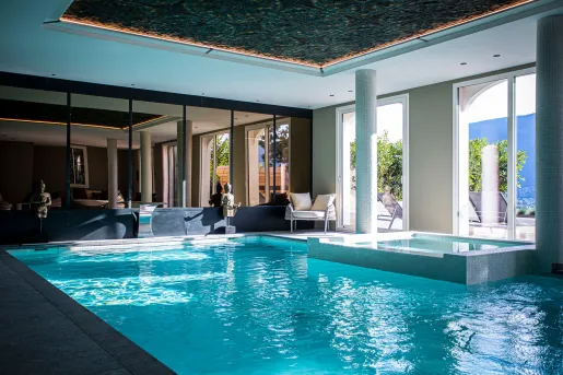 Indoor swimming pool with large mirrors and windows with views of an outdoor patio