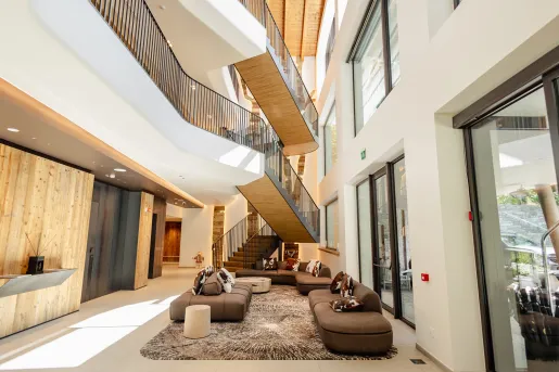 Interior view of tall hotel lobby with large staircase and brown sofas on the ground floor