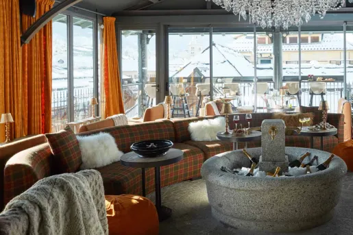 Open room with large windows and a plaid, circular couch, with a large stone fountain with bottles of champagne