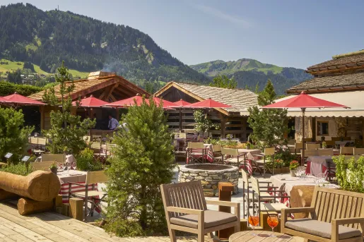 Outdoor patio with red umbrellas and wooden cabins in the background
