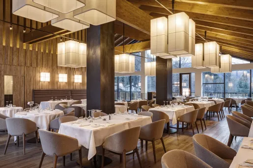 Indoor restaurant dining area with long tables with white table cloths, with cushioned gray chairs surrounding