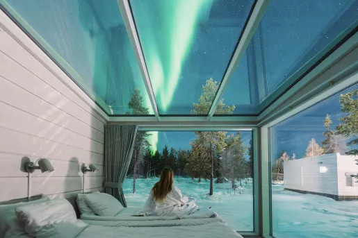 Woman sitting in a glass room looking up at the northern lights