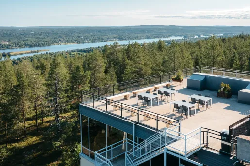 Sky view of building rooftop with chairs and tables, looking out to tall trees