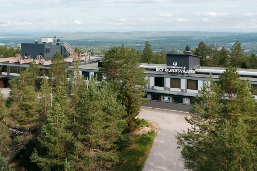 Exterior view of gray and white hotel building, with tall trees in front