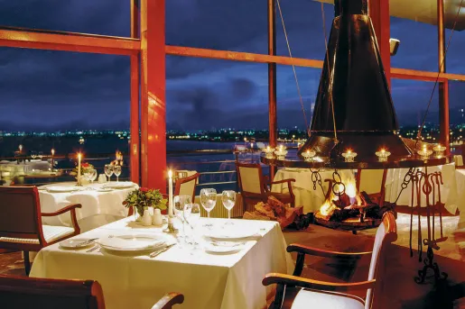 Restaurant dining area with white dining tables and wine glasses on each table, with large glass walls