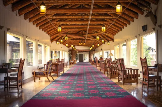 Long hallway with a long rug and cushioned chairs on either side looking out to large windows