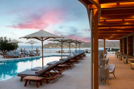 Outdoor pool surrounded by reclining chairs and the ocean in the background
