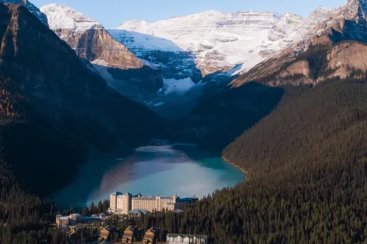 Large valley of trees, with a lake in the center and snow-capped mountains in the background
