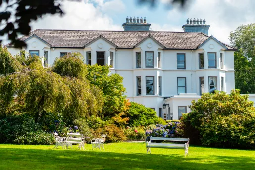Exterior view of white building with large trees and a grass field in front