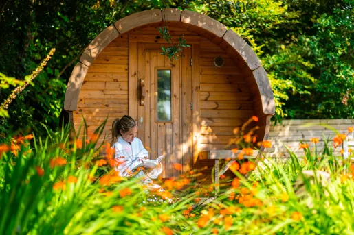 Woman sitting in front of a wooden cabin building, reading a book