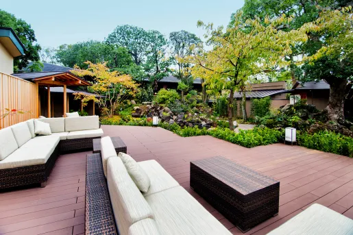 Outdoor patio with cushioned sofas, surrounded by tall green and yellow trees