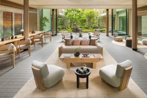 Outdoor patio with cushioned, white chairs and wooden tables, with a garden in the backrground