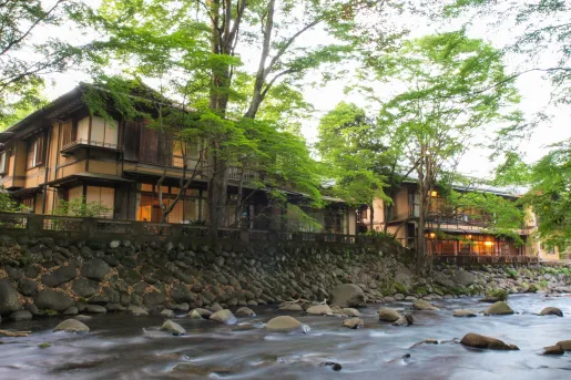 Exterior view of Japanese-style building on a small hill, with a river in front